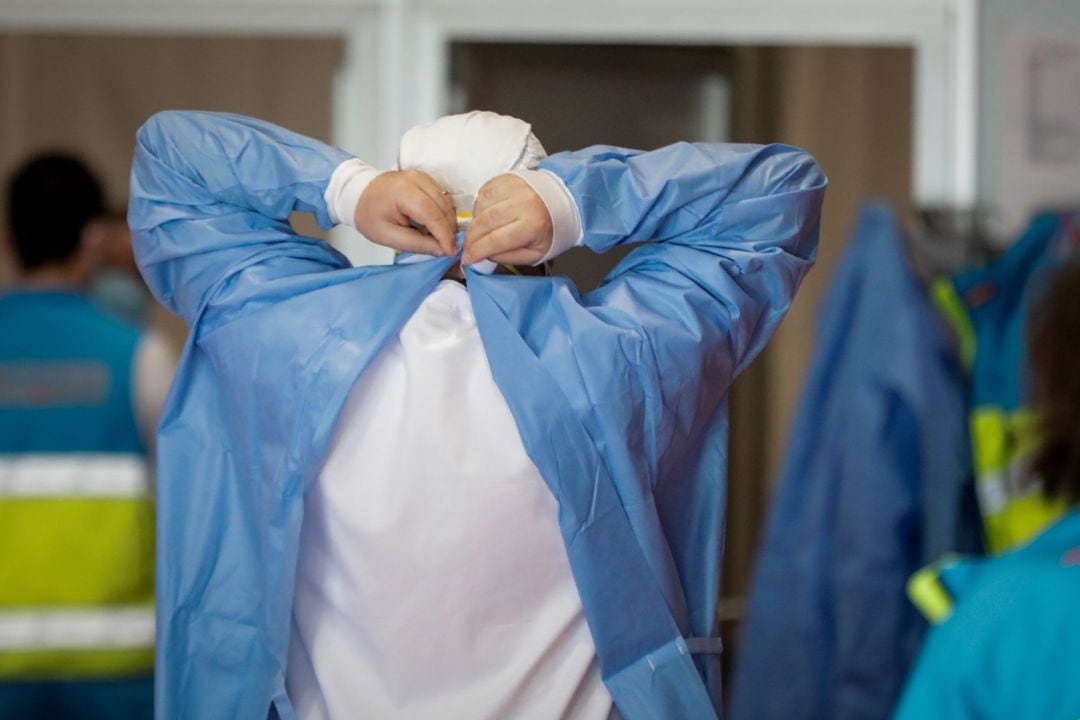 Un sanitario se pone la bata protectora antes de iniciar su jornada laboral.