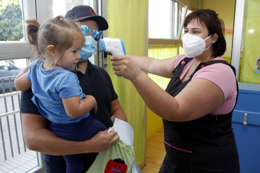 Una professora mesurant la temperatura a una nena que acaba d&#039;arribar al centre, el 8 de juny de 2020