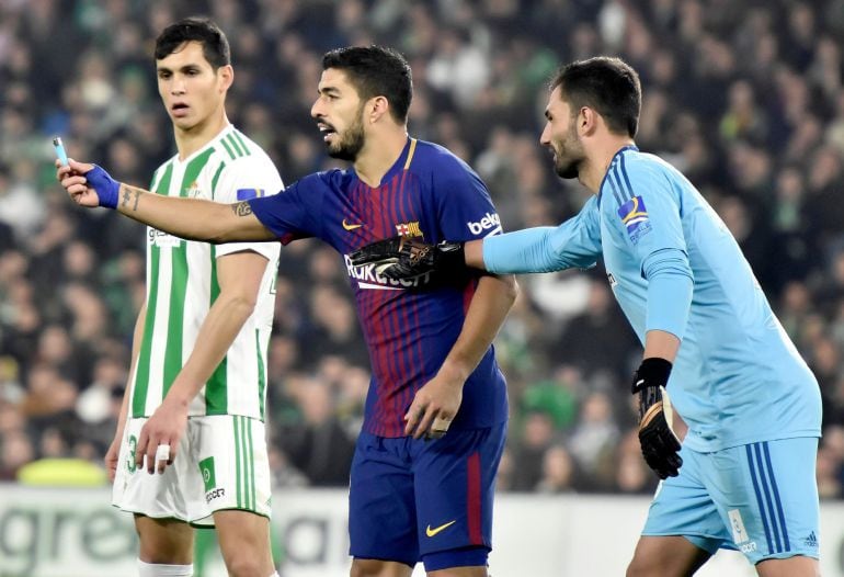 Luis Suárez muestra al árbitro ante los jugadores del Betis un mechero lanzado al campo de juego