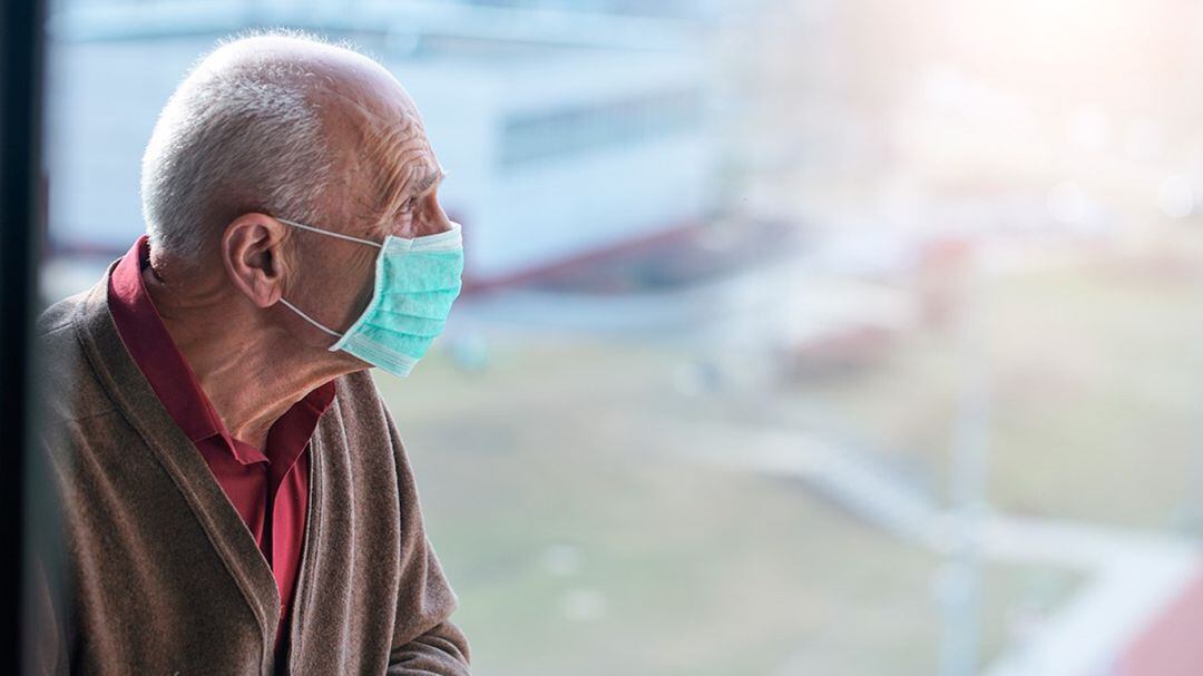 Un anciano con mascarilla mira al horizonte.