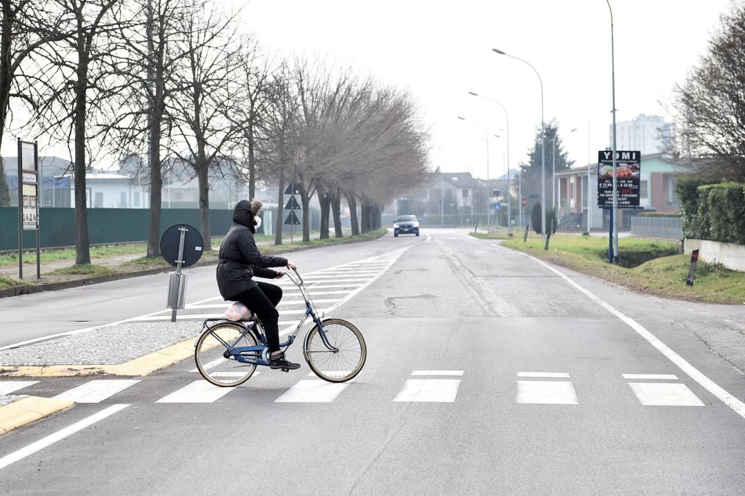 Una persona con mascarilla cruza en bicicleta la ciudad de Codogno, en Italia