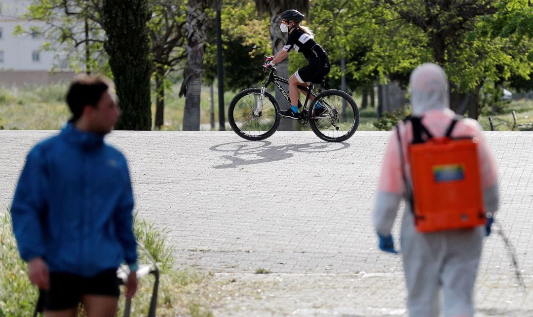 Un ciclista, un corredor y un desinfectador recorren el antiguo cauce del Turia dentro de la nueva normativa decretada por el Gobierno que permite hacer deporte o salir a pasear en dos franjas horarias.