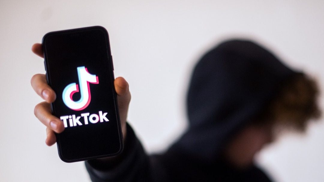 Un jóven sujetando su móvil en el que se ve el logotipo de Tik Tok.