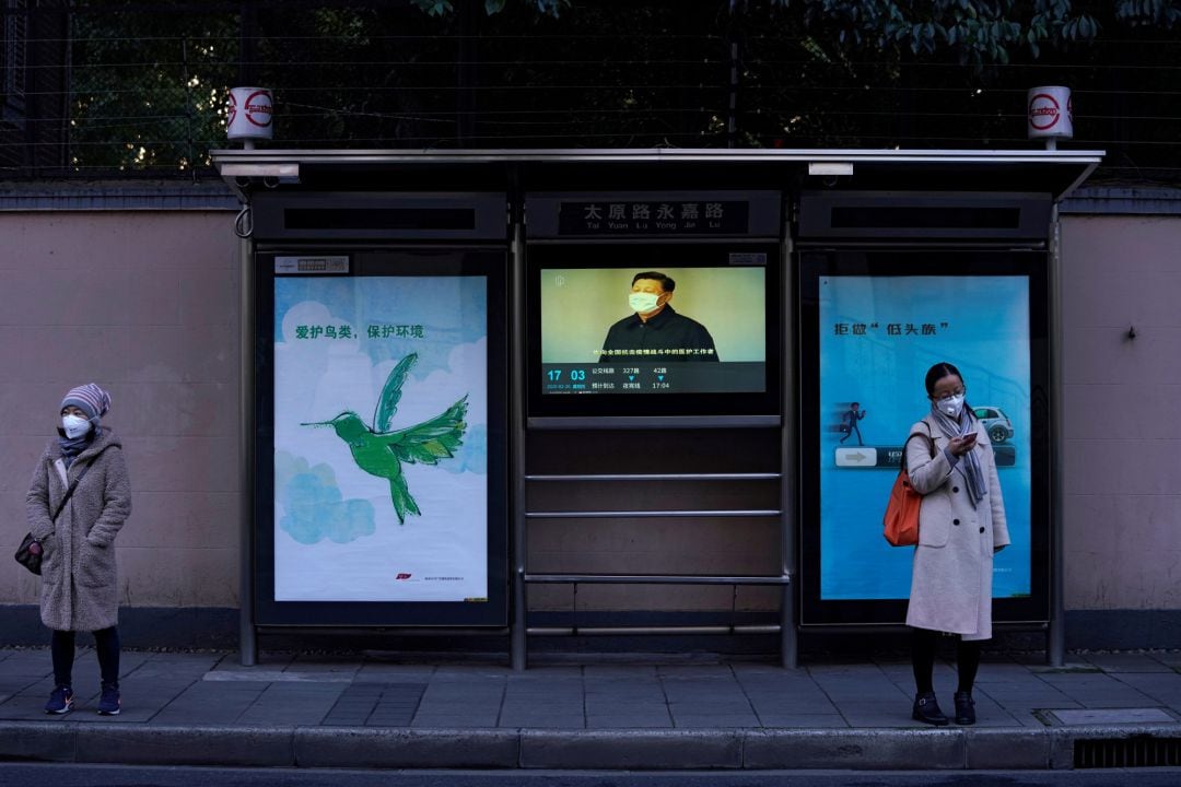 Una mujer lleva mascarilla delante de una televisión donde se ve al presidente Xi Jinping con otra