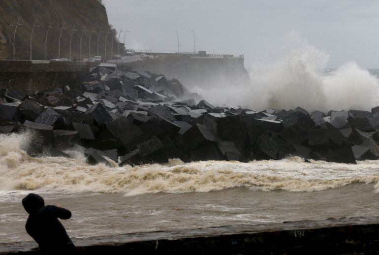  Un hombre toma fotografías del paseo Nuevo de San Sebastián desafiando a la lluvia y al viento