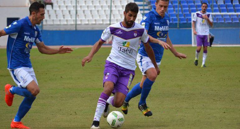 Dos jugadores de la Unión Deportiva Melilla intentan quitar el balón a un futbolista del Real Jaén.