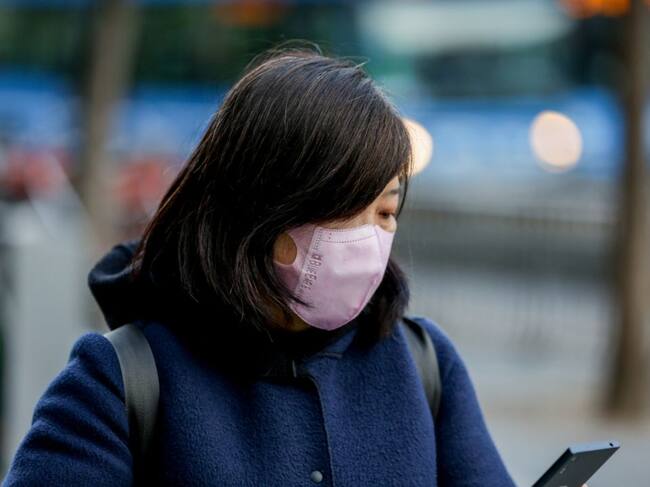Una mujer asiática mira su móvil con una mascarilla protectora, mientras las farmacias registran una alta demanda de estas por parte de ciudadanos chinos tras el coronavirus, en Madrid (España), a 30 de enero.