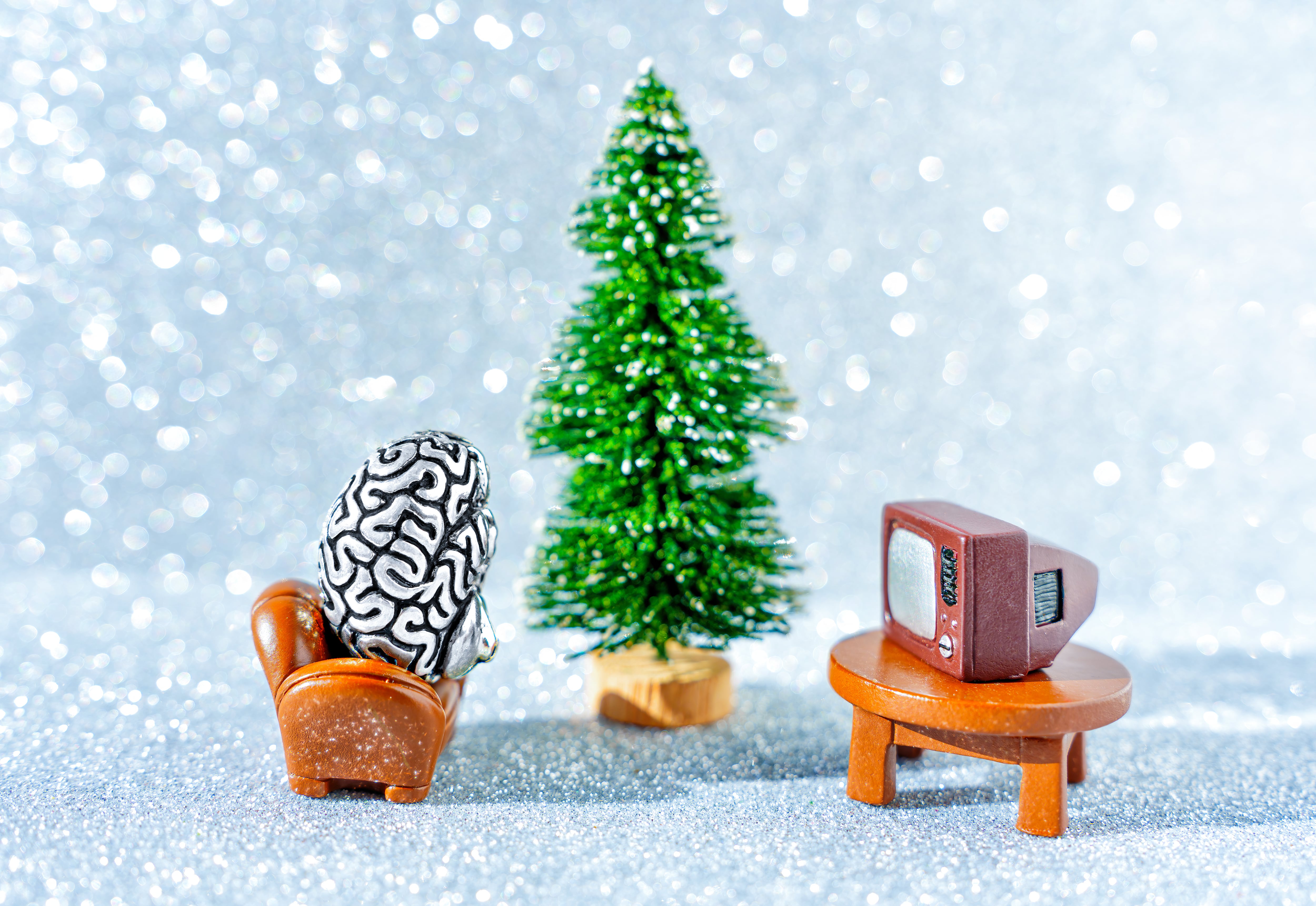 Creative Christmas brainwashing concept: anatomical copy of a human brain watching TV sitting in a chair by a new year tree.