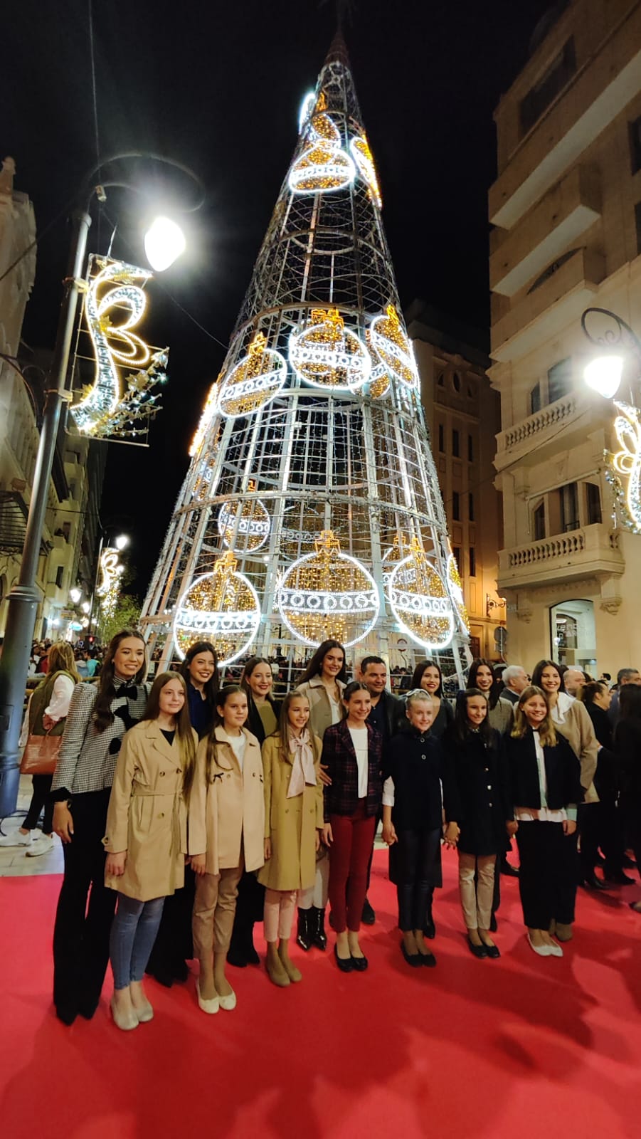 Las Belleas del Foc, junto con representantes de las Hogueras, posando delante del árbol iluminado