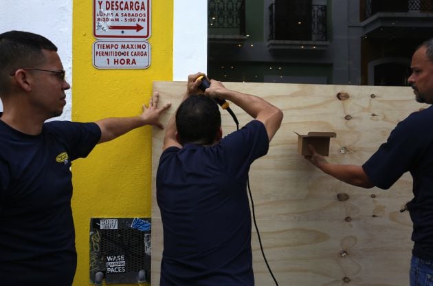 Unos hombres cubren la entrada de un local con tablas de madera este martes en San Juan (Puerto Rico)