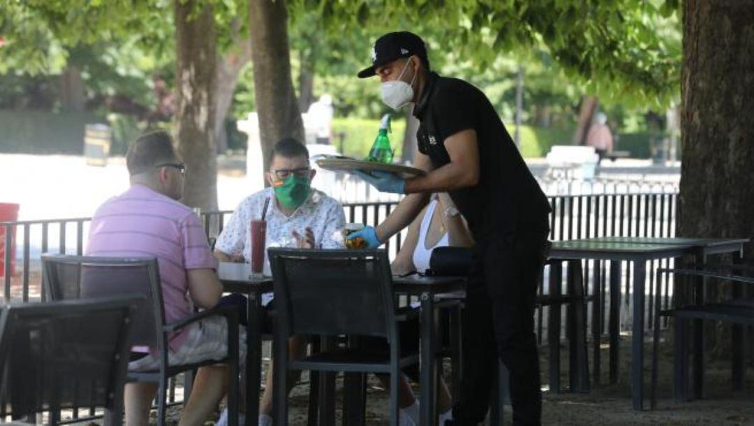 Un camarero protegido con mascarilla atiende a una mesa de una terraza