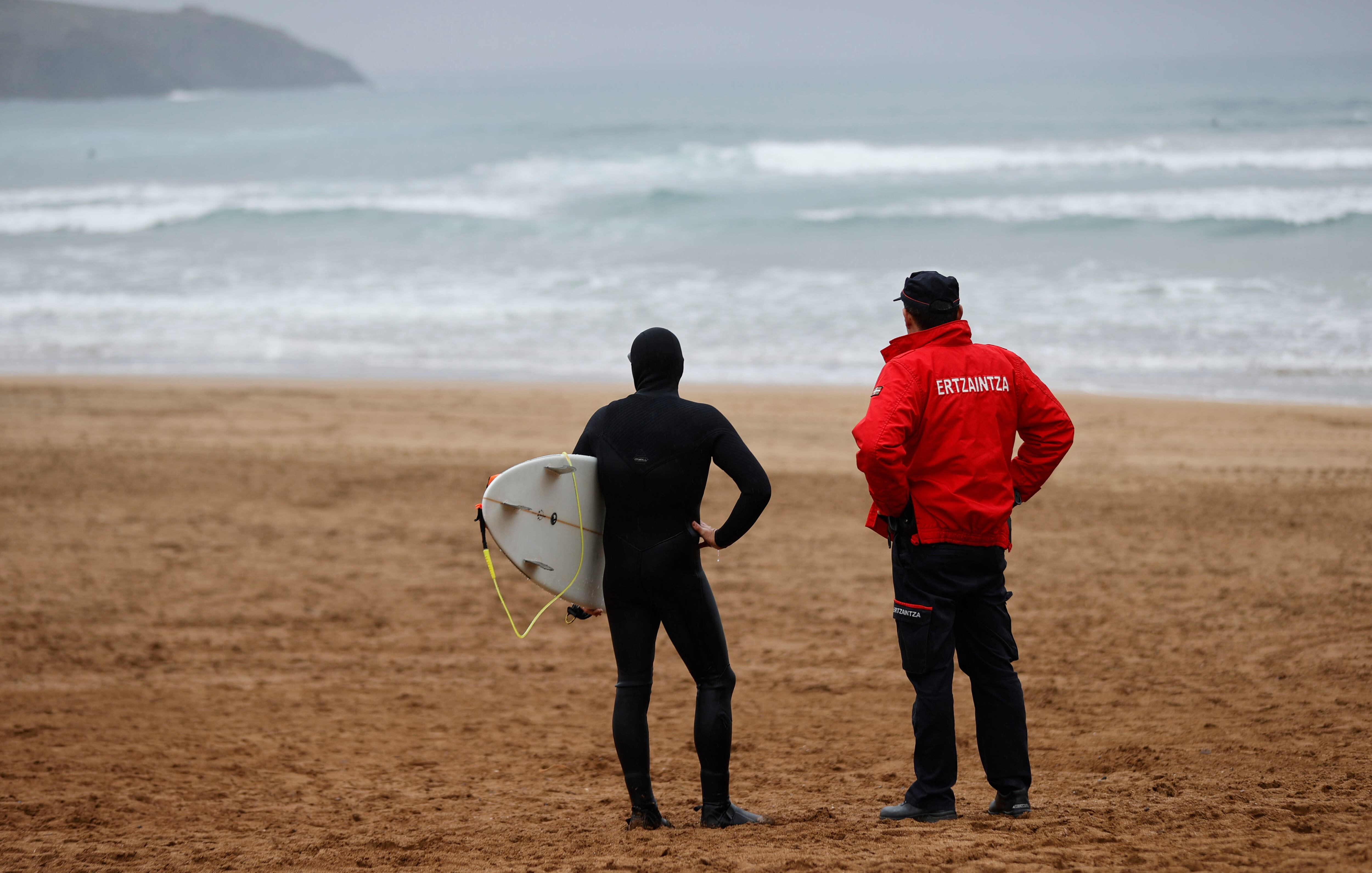 Un ertzaina pregunta al salir del agua a un surfista si ha visto bolas de plástico en la playa vizcaína de Muskiz. La consejera de Desarrollo Económico, Sostenibilidad y Medio Ambiente, Arantxa Tapia, ha afirmado este miércoles que hasta mañana &quot;no habrá datos concluyentes&quot; para saber si el material recogido en la playa de Muskiz  procede del vertido de pellets de Galicia. EFE/Luis Tejido