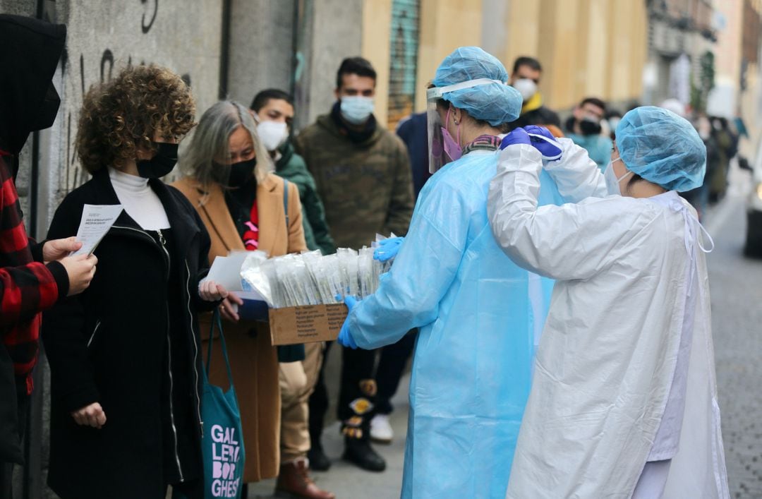 Una sanitaria pone el EPI a otra sanitaria para recoge test de COVID-19 de las personas que hacen cola en el Centro de Salud Universidad en Madrid