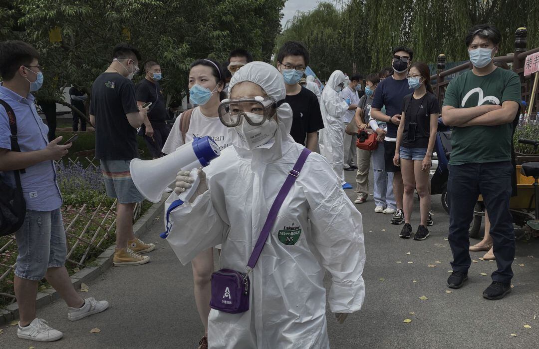 Una trabajadora del servicio de control epidemiológico de China, con traje protector informa por las calles de Pekín que realizarán pruebas a todas las personas que hayan estado en las inmediaciones del mercado de Xinfadi donde se detectó el foco de un nuevo rebrote en el país asiático. 