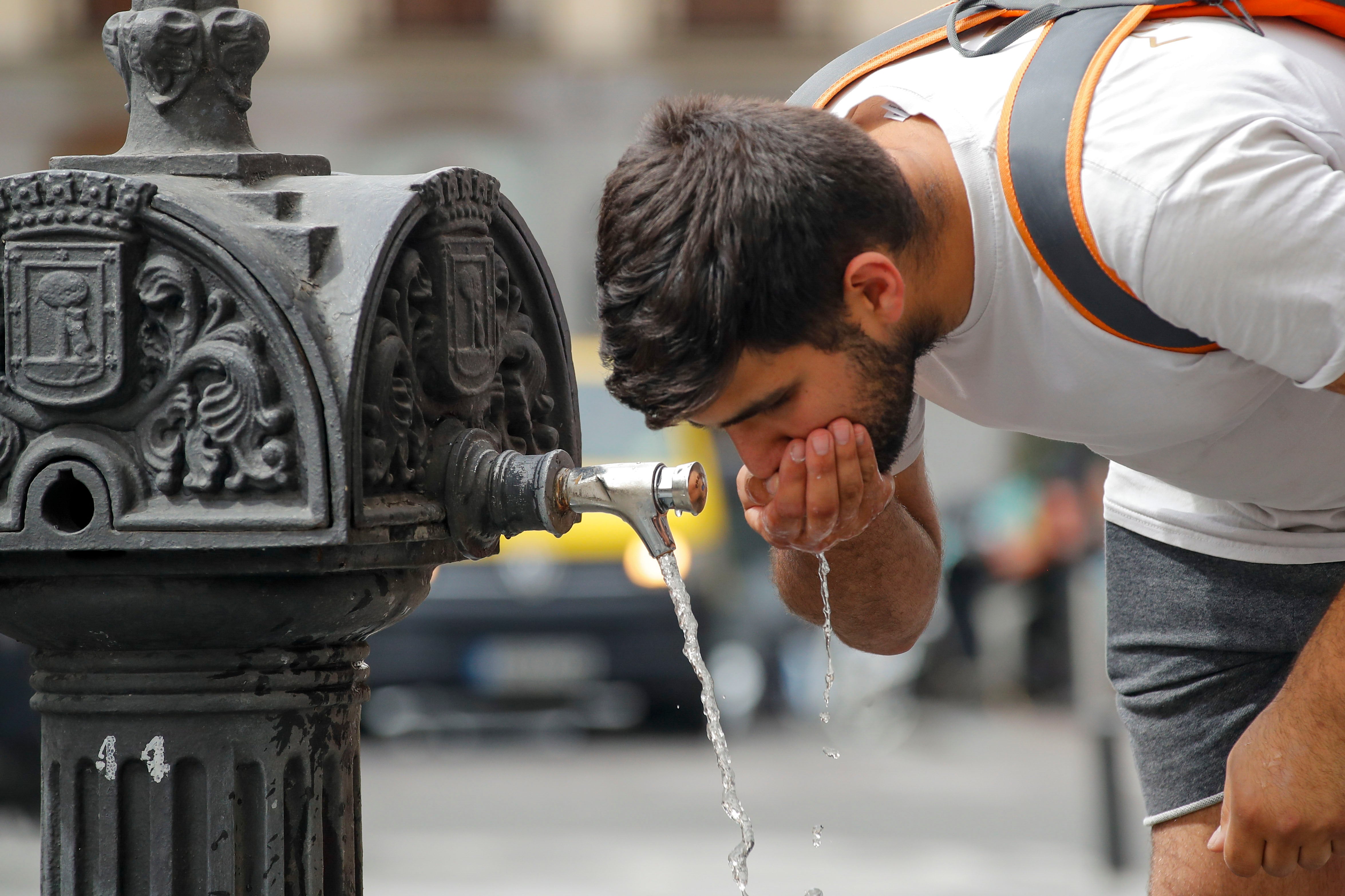 Un hombre bebe agua en una fuente pública del centro de Madrid,.