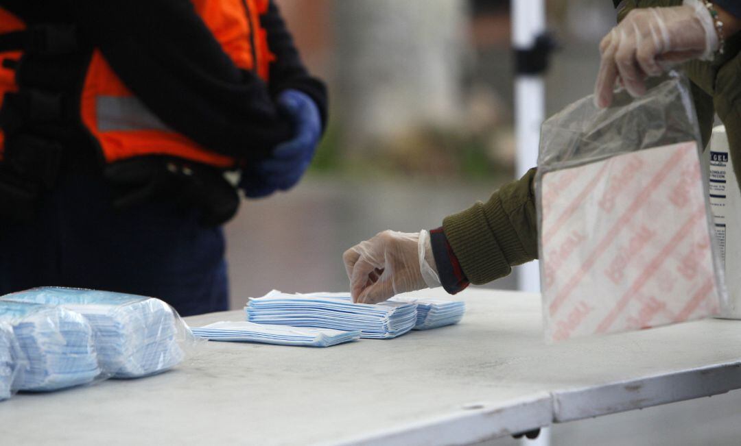 Transeúntes recogen mascarillas puestas a disposición de los peatones en una mesa instalada en una calle.