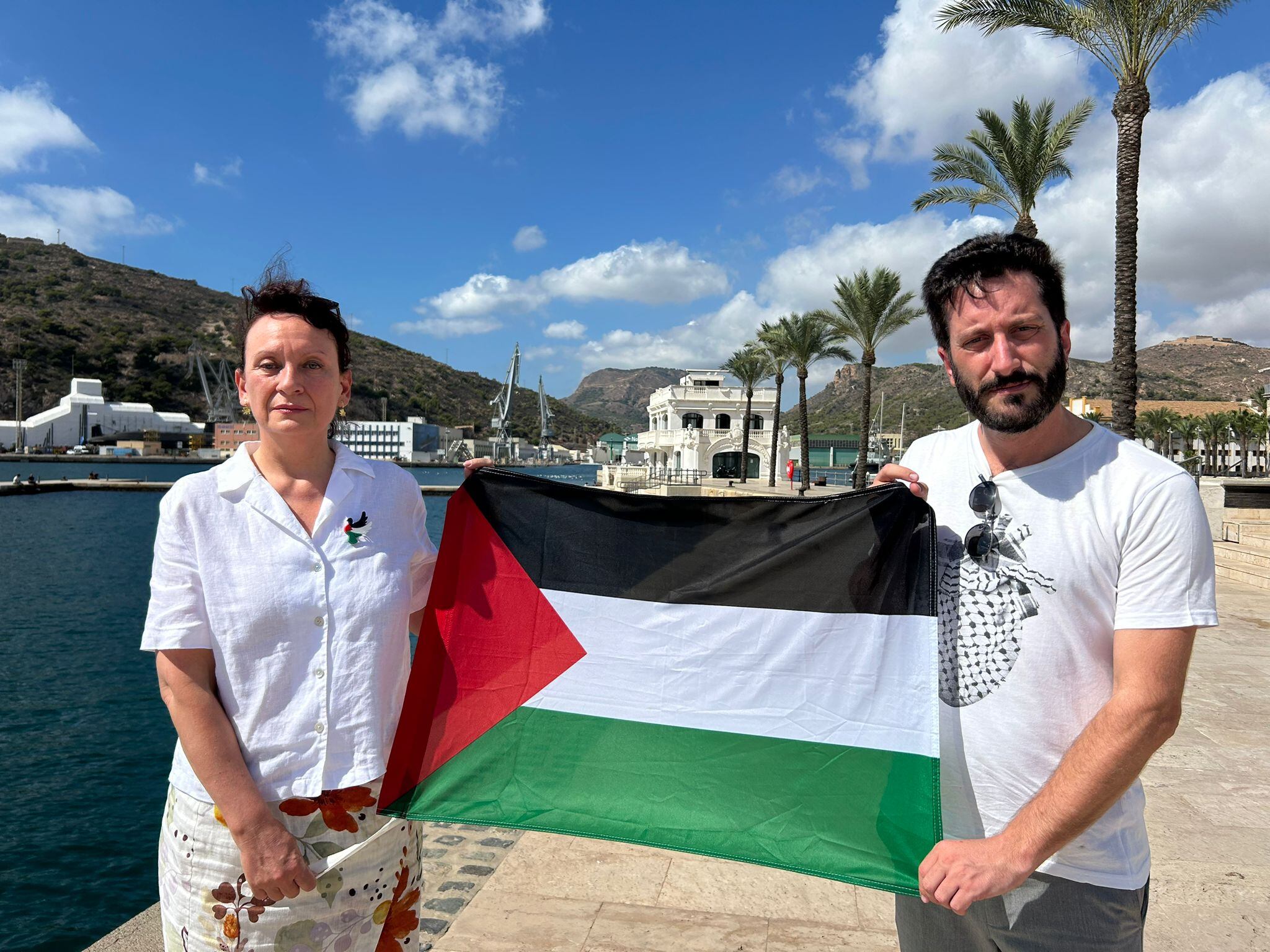 María Marín, diputada de Podemos y Víctor Egío, secretario de la formación, portan la bandera de Palestina en el Puerto de Cartagena