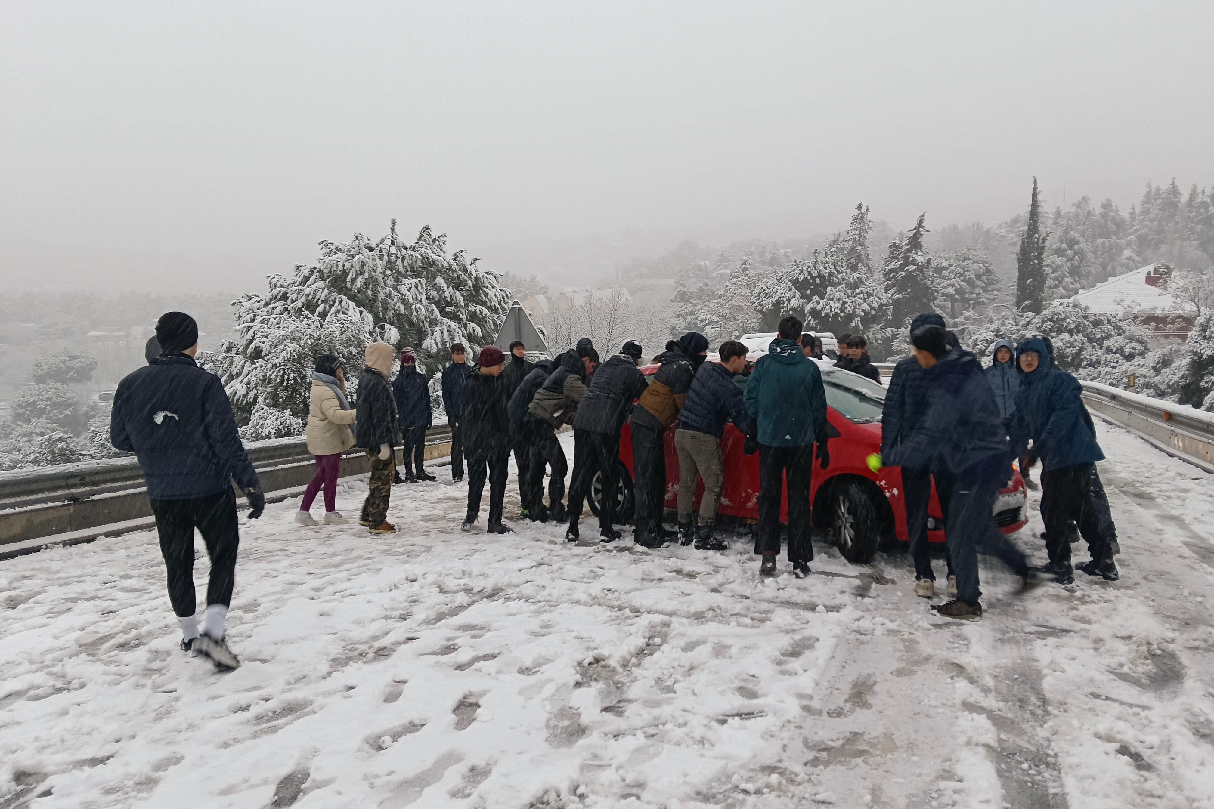 Varias personas tratan de mover un vehículo atravesado en la carretera M-519 a la altura de Galapagar, en el que la borrasca Kristin deja nieve en la región de Madrid.