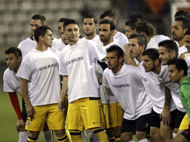 Los jugadores de L'Hospitalet y del Atlético de Madrid lucen camisetas antiviolencia antes de comenzar el partido de ida de dieciseisavos de final de la Copa del Rey.