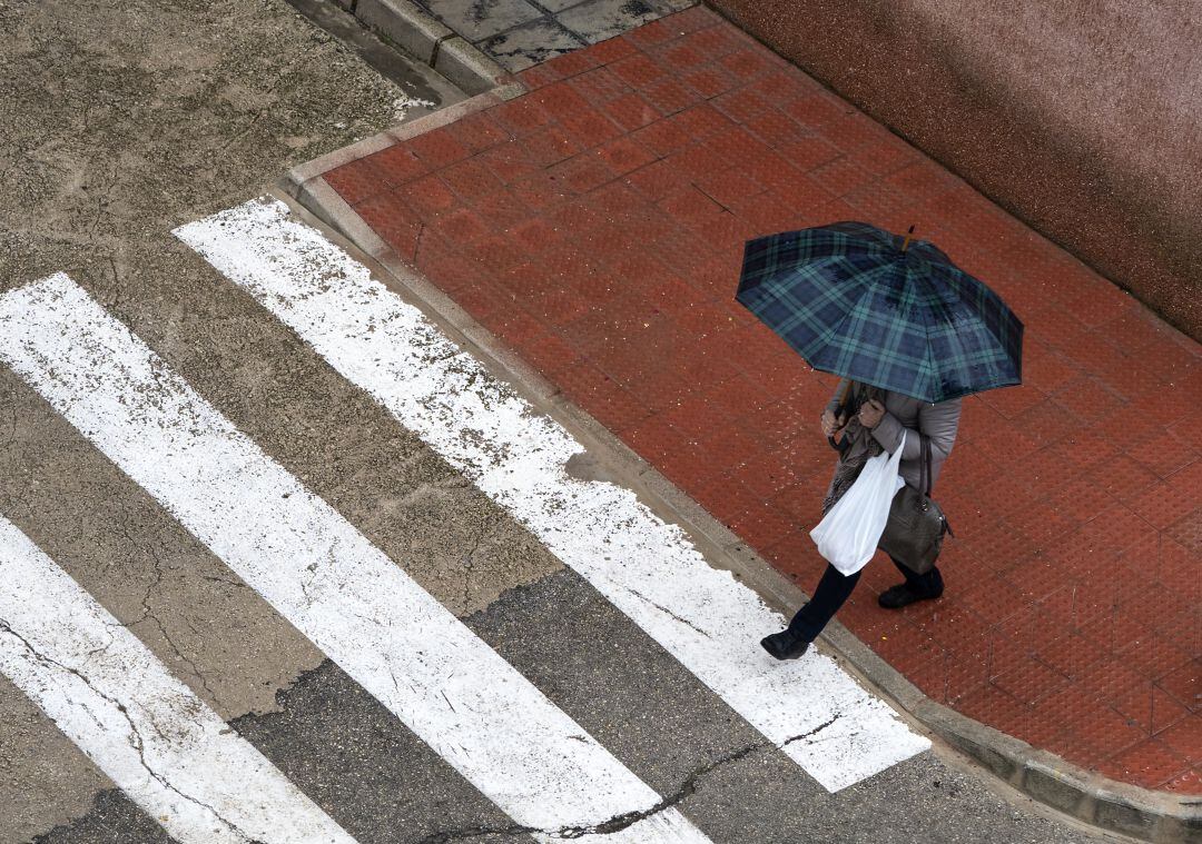 Foto de archivo de una persona atravesando un paso de cebra en un día de lluvia en València