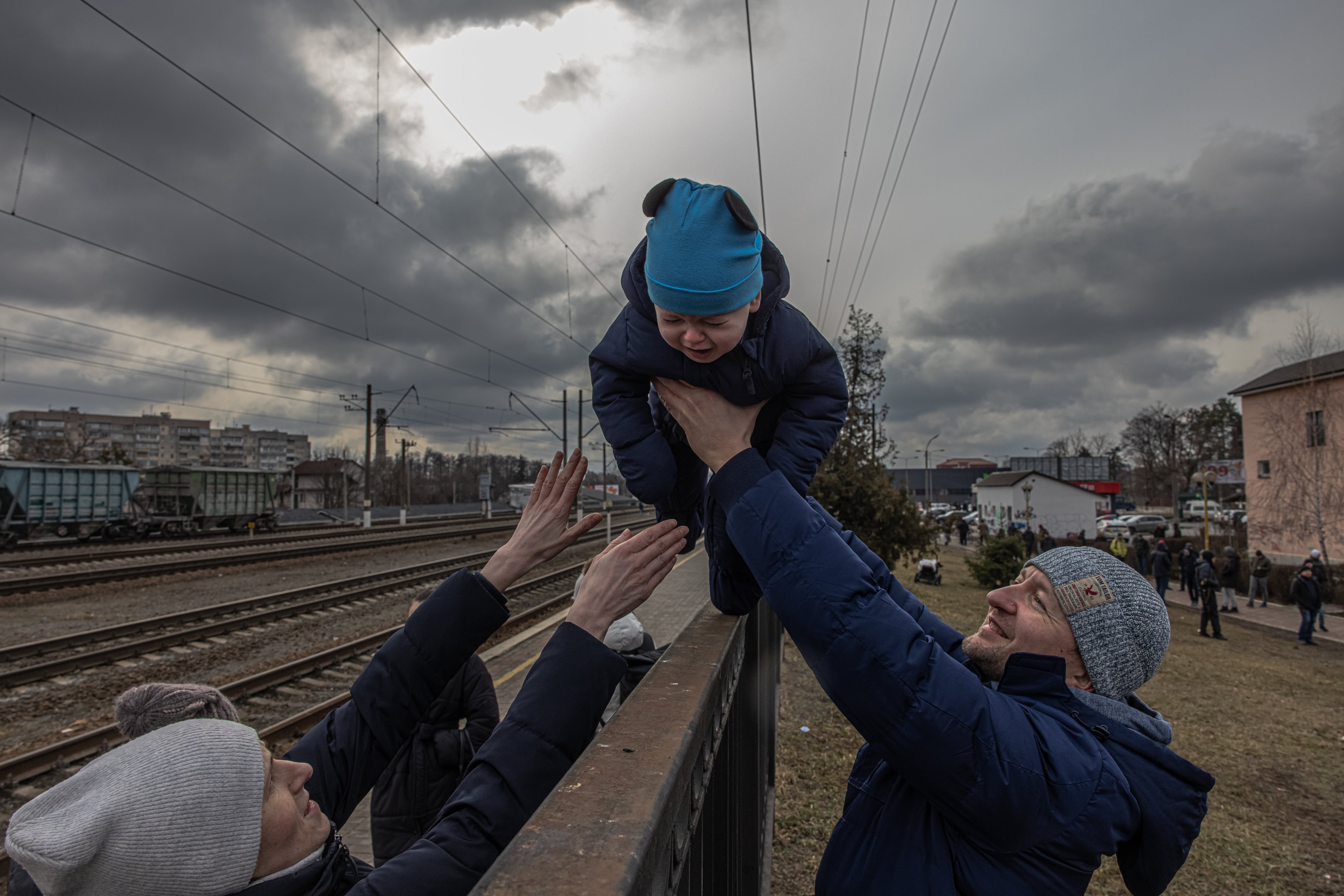 Oleg (d), un padre ucraniano que decidió no abandonar  Irpin, pasa a su hijo por encima de una verja para entregárselo a su mujer, Yana, antes de la llegada de un tren de evacuación a la estación de Irpin, el 4 de marzo de 2022.