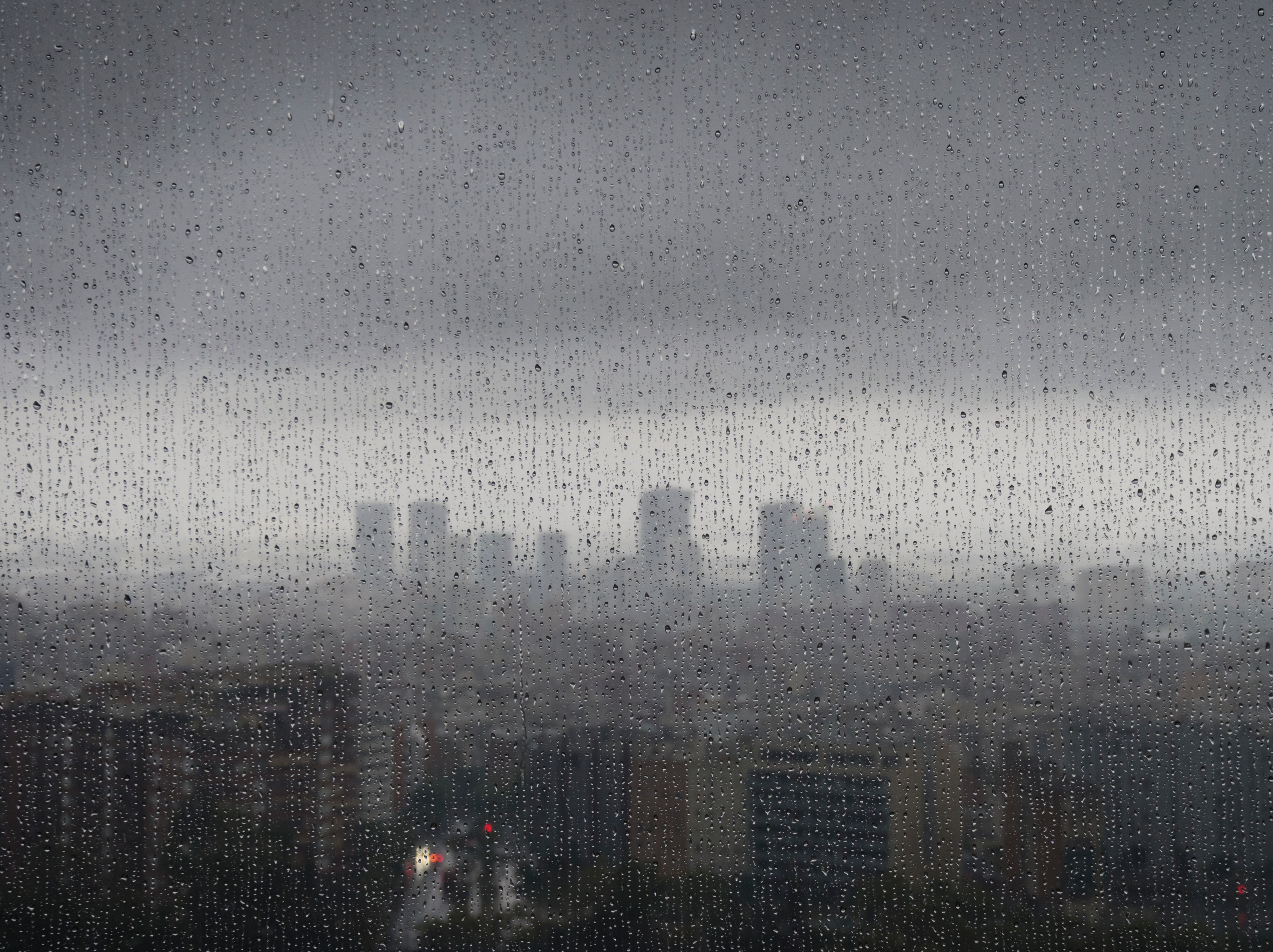 After heavy rainfall, the diffuse skyline of Barcelona is emerging in the twilight behind raindrops on a window.