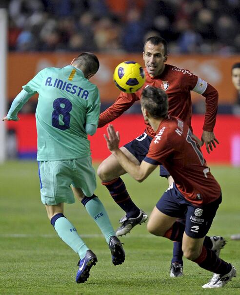 El centrocampista del FC Barcelona Andrés Iniesta (i) cabecea el balón ante el jugador del Osasuna Francisco Puñal (c-atrás) durante el partido correspondiente a la decimocuarta jornada de Liga que ambos equipos disputan en el estadio Reyno de Navarra