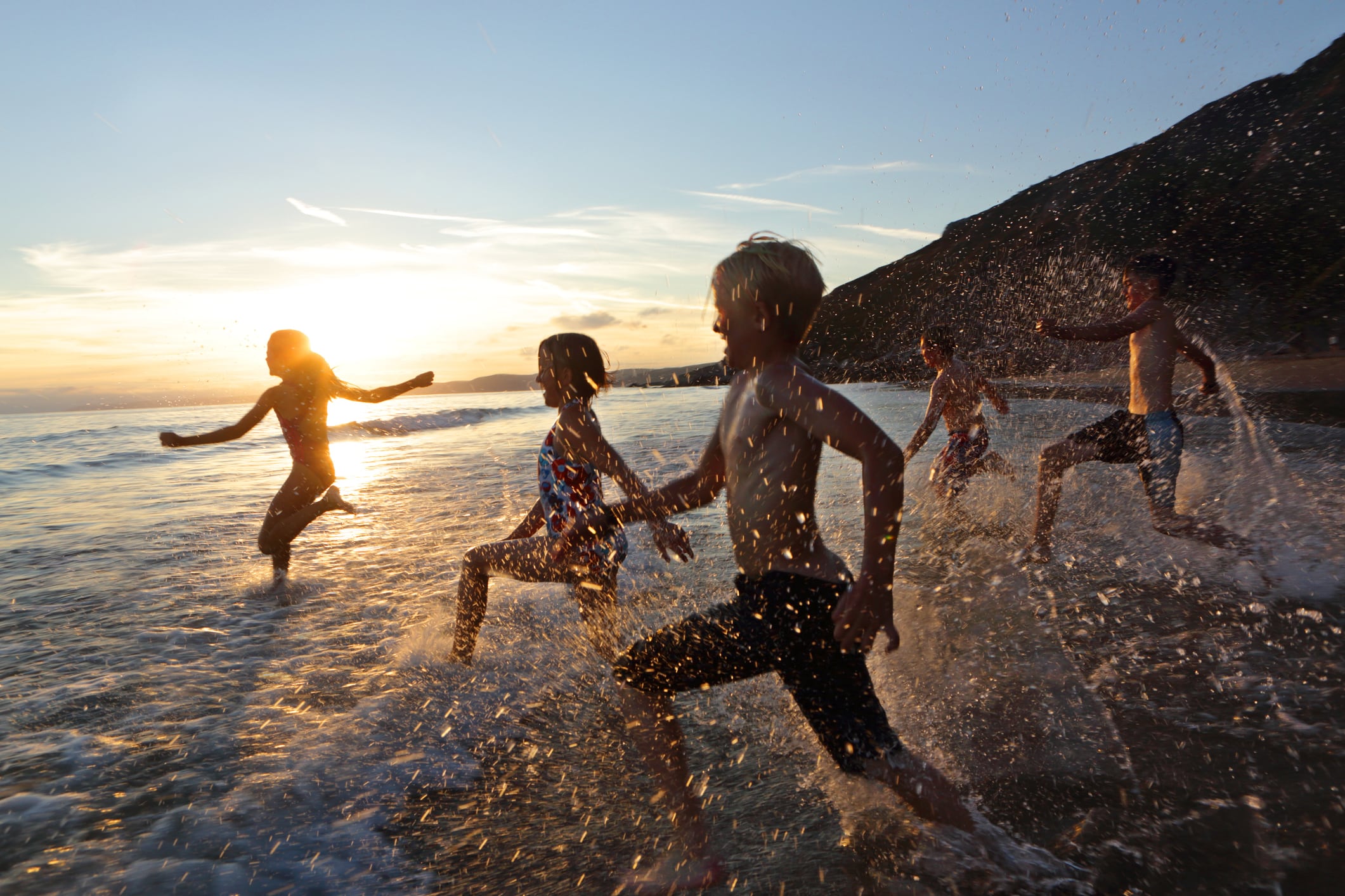 Varios niños y niñas corriendo en la playa.