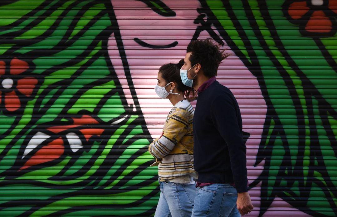 Un hombre y una mujer pasean con la mascarilla puesta.