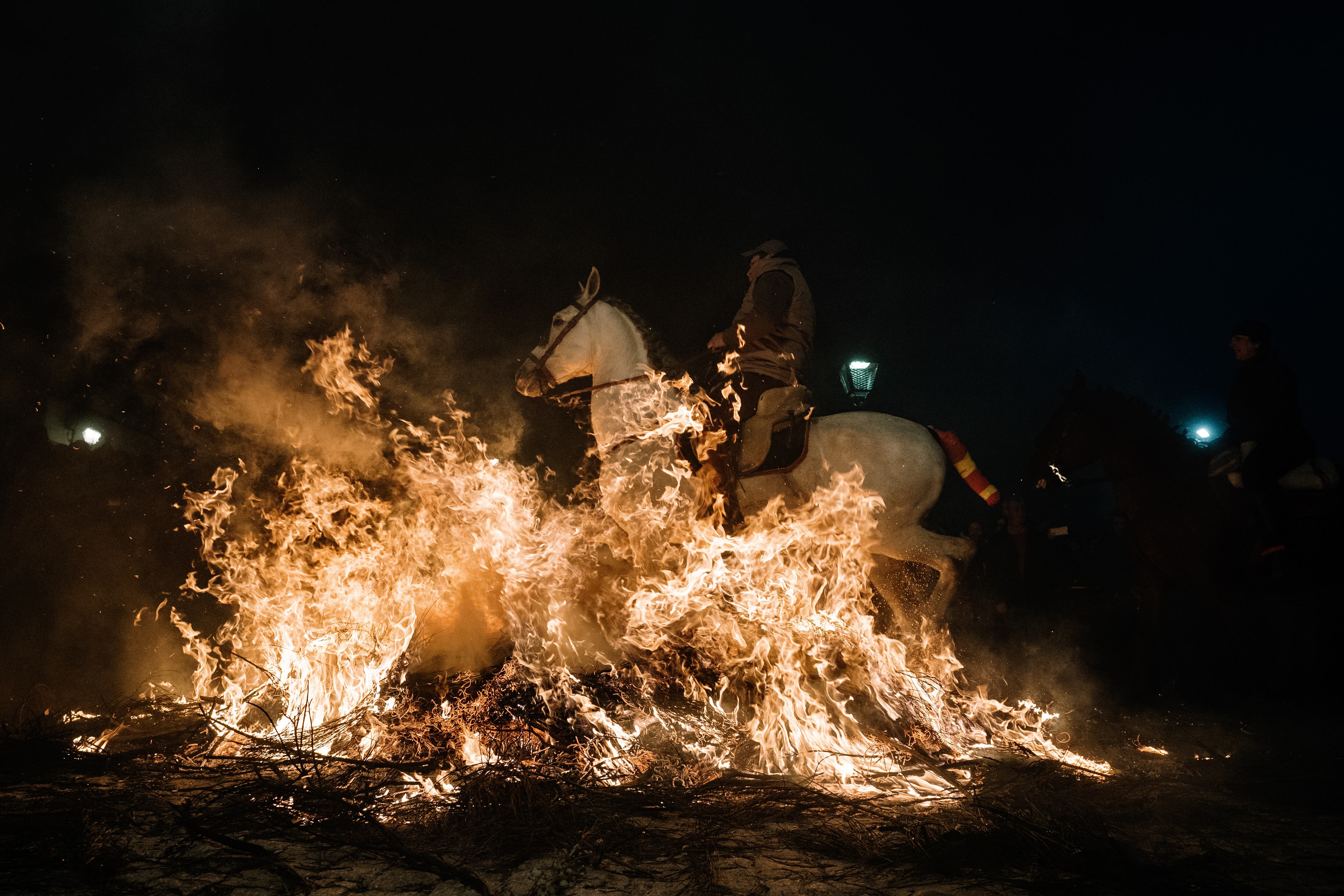 Un jinete pasa con su caballo por encima de las llamas durante las tradicionales &quot;luminarias&quot; que se celebran  en la localidad abulense de San Bartolomé de Pinares.