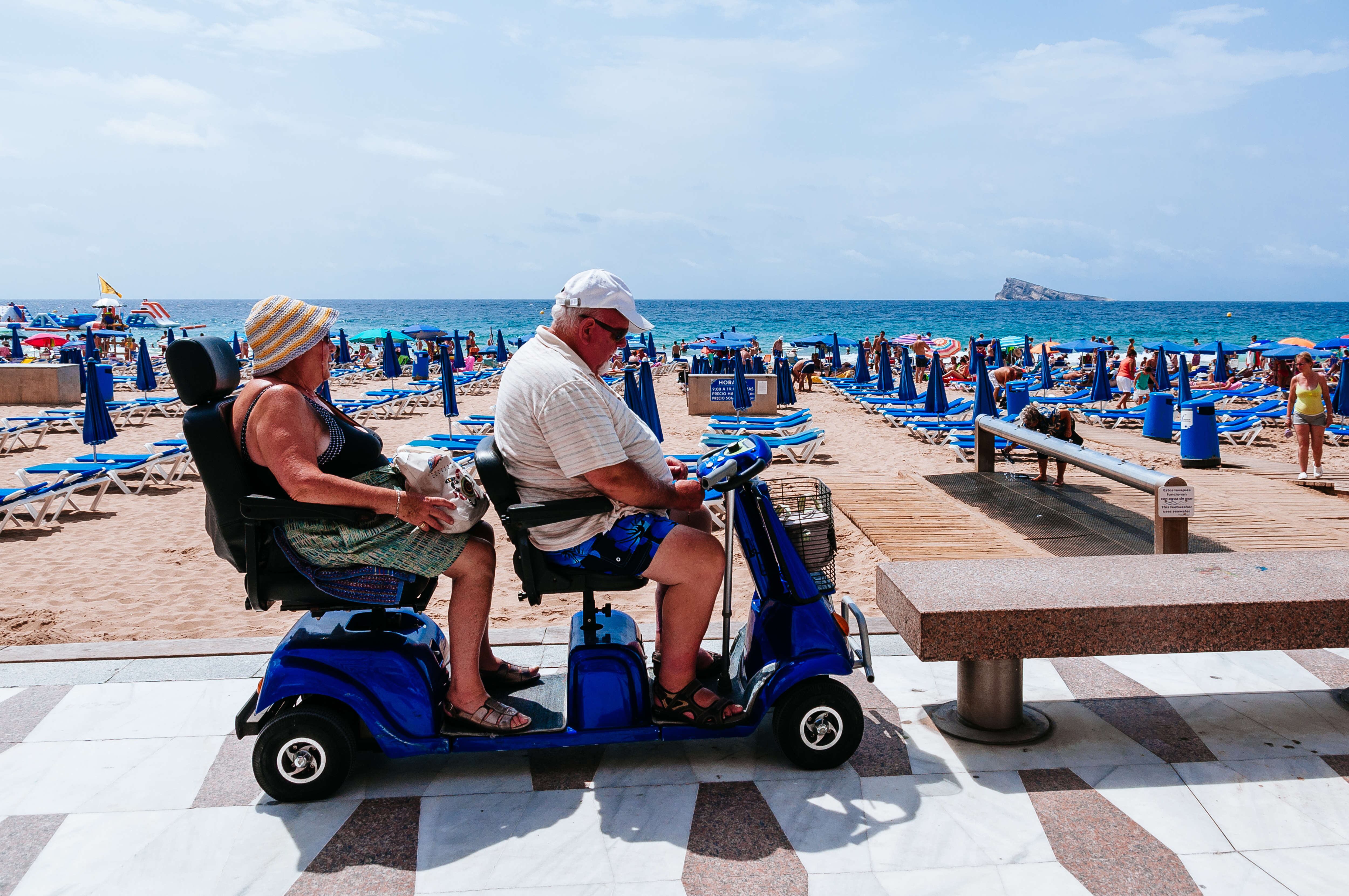 Una pareja atraviesa el paseo marítimo de Benidorm con una motocicleta tipo &#039;scooter&#039;.