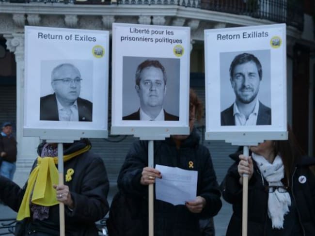 Persones amb llaços grocs aguantant tres pancartes amb les cares de Puig, Comín i Forn a Reus