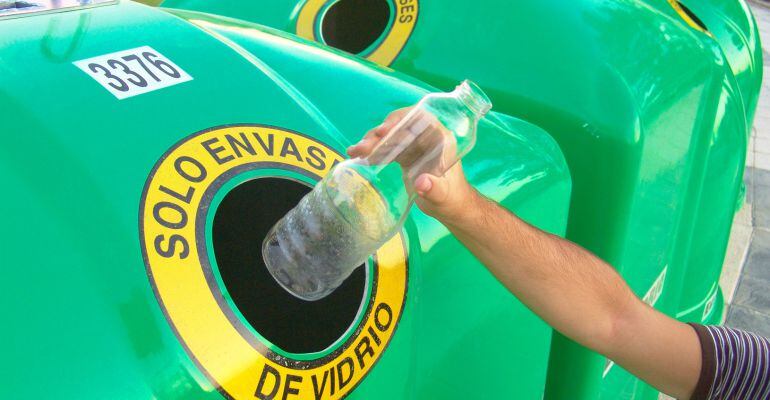 Una persona introduce una botella de vidrio en un contenedor de reciclaje de vidrio.