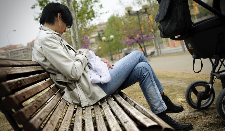 Una madre da de mamar a su hijo en un parque.