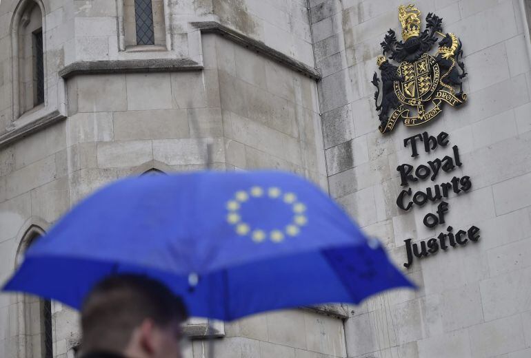 Un hombre con un paraguas con la bandera de la Unión Europea pasa por delante del Tribunal Superior de Londres (Reino Unido