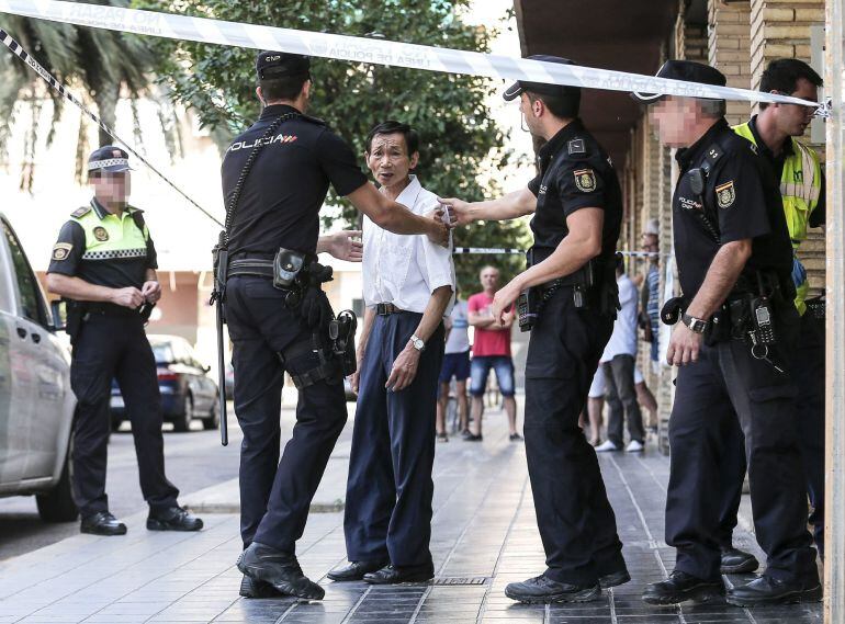 Varios agentes de policía acompañan a un hombre mayor a las puertas del número 21 de la calle Villarroya de Valencia donde se han encontrado los cuerpos acuchillados de una mujer de unos 45 años y una niña de alrededor de 10.