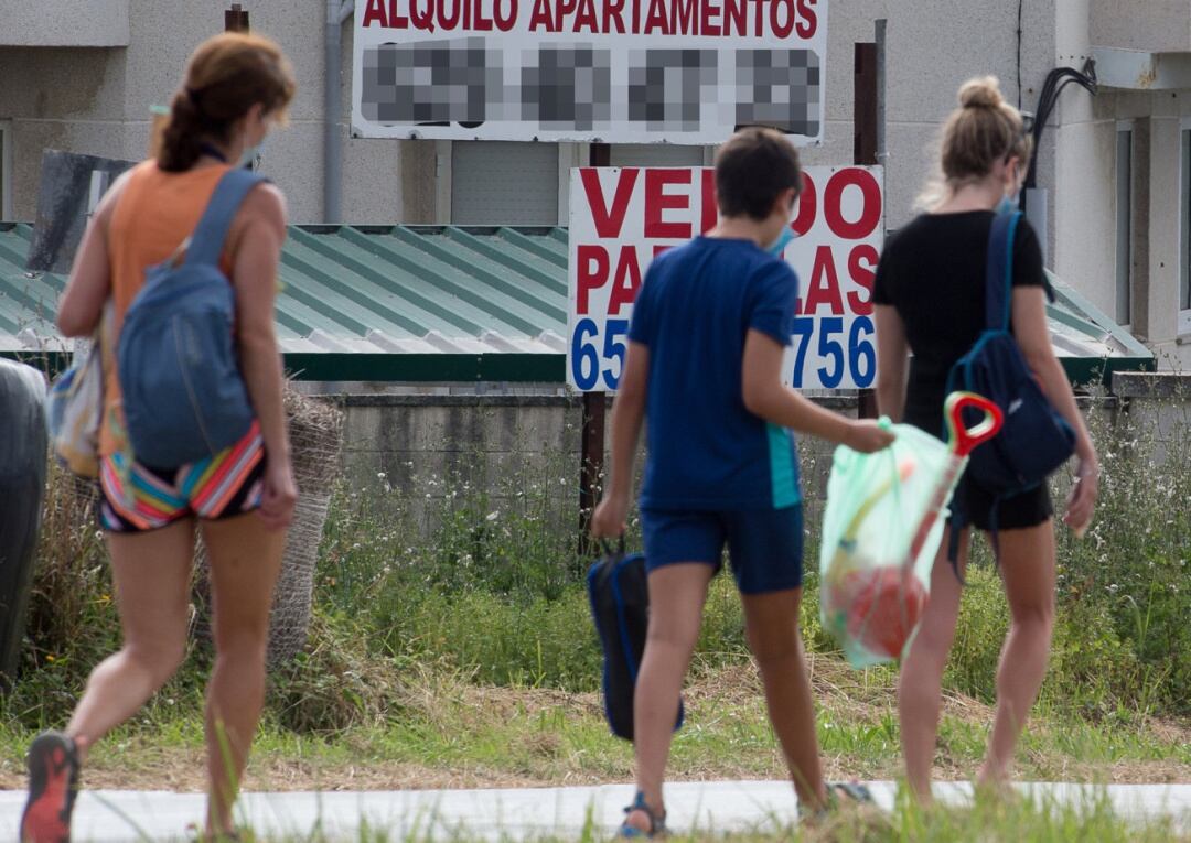 Tres personas caminan junto a varios carteles de viviendas en venta y en alquiler en A Mariña