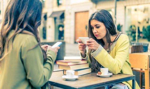 Dos chicas consultan su teléfono móvil.