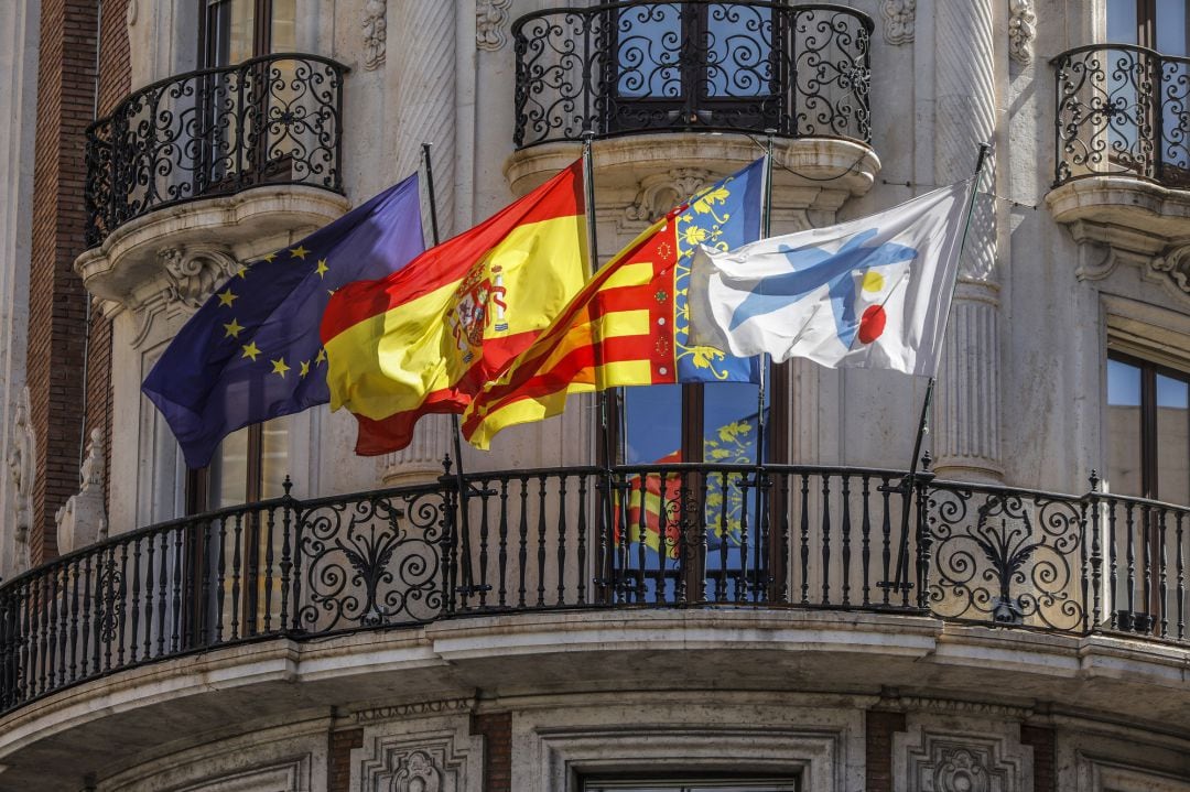 Banderas de la UE, España, Comunidad Valenciana y Caixa ondeando en los balcones de la sede de Caixabank, en València