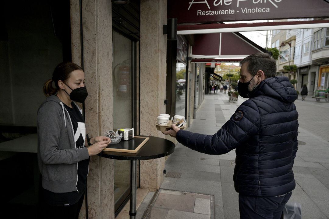 Un hombre recoge unos cafés de un establecimiento con las nuevas restricciones para la hostelería.