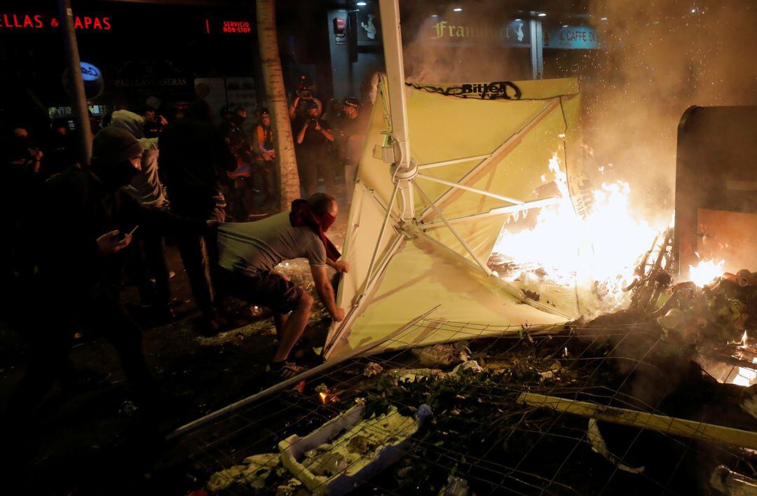 Un radical arroja una sombrilla a una hoguera callejera para reavivarla.