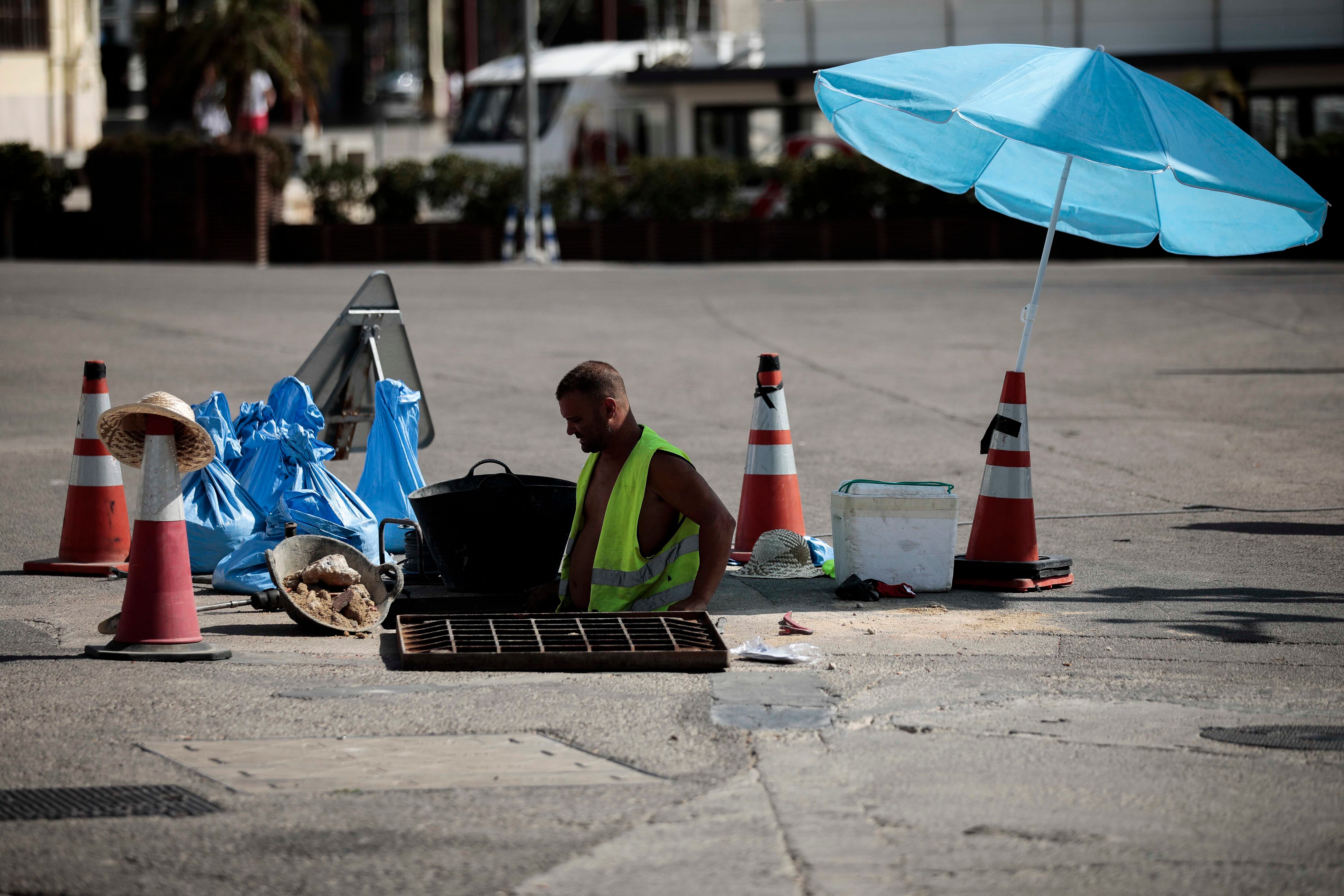 Un trabajador se protege del sol con una sombrilla en Valencia.