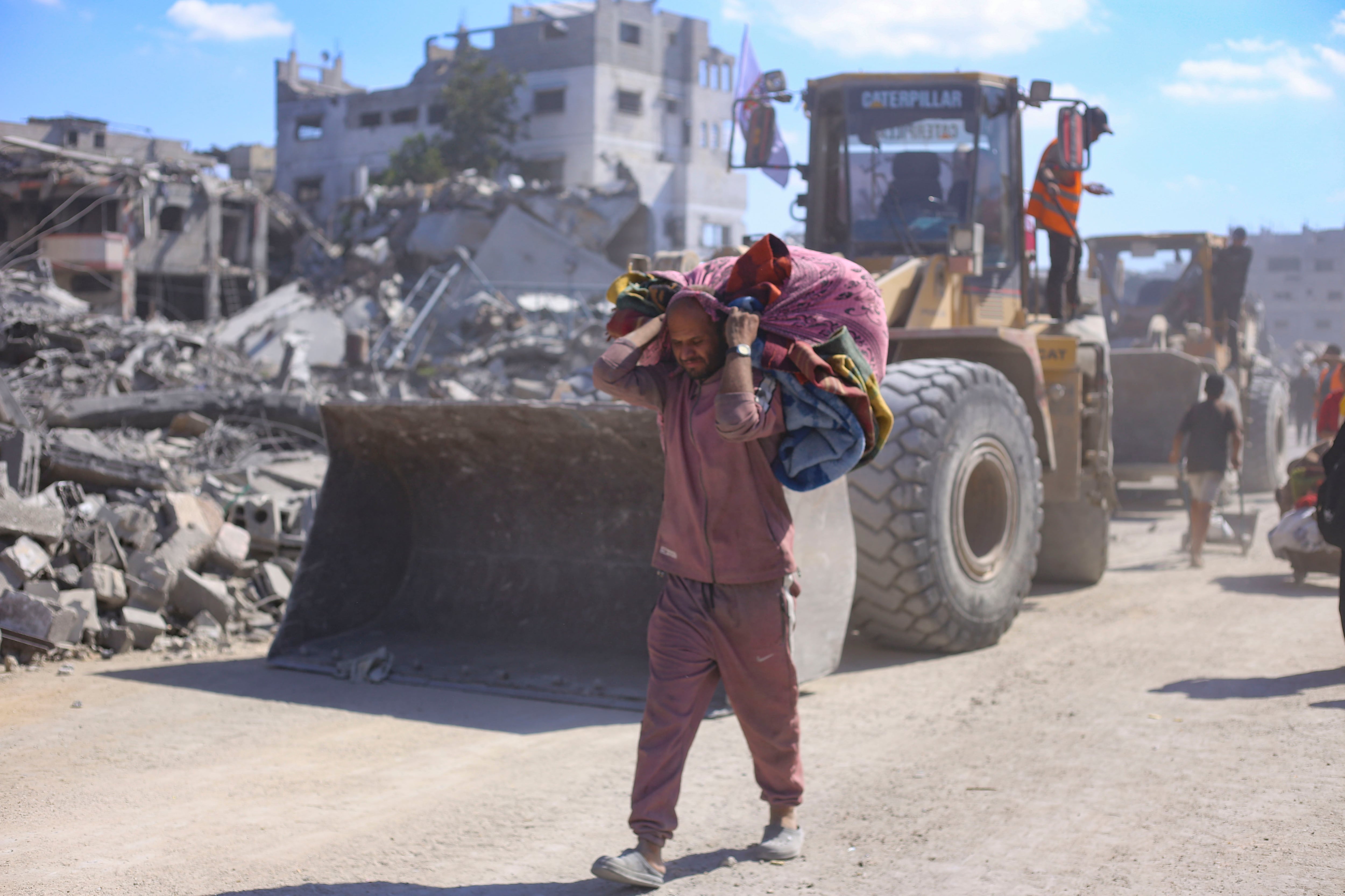 Un hombre con un hatillo con sus pertenencias pasa ante varias excavadoras del Ayuntamiento de la ciudad de Gaza que comienza este martes las operaciones de remoción de escombros y apertura de las calles principales de la capital gazatí para despejarlas y prepararlas para su uso, tras dos años de bombardeos. La reconstrucción de la Franja de Gaza, donde la destrucción es casi completa, requerirá al menos 70.000 millones de dólares, de los cuales 20.000 millones deben ser invertidos en los próximos tres años para hacer viable la vida en este territorio palestino. EFE/ Ahmad Awad
