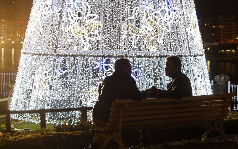 Dos personas conversan junto a un árbol de navidad gigante, junto al palacio de Miramar de San Sebastián.