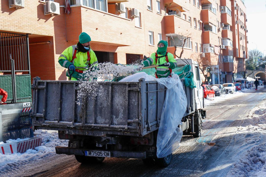 Dos operarios lanzan sal para el acondicionamiento de calles en Valdemoro (Madrid).