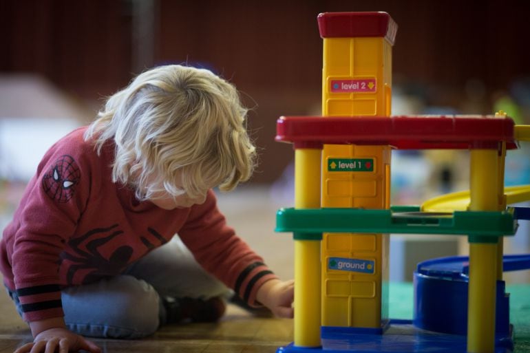 Un niño juege en el suelo a los coches. 