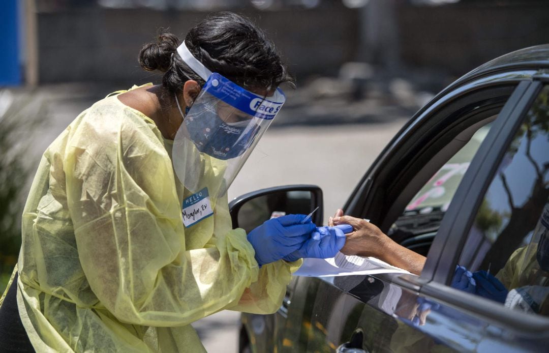 Una asistente sanitaria realiza una prueba de coronavirus a una persona desde el interior de su vehículo en Los Ángeles, Estados Unidos.