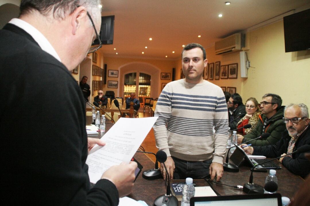 Juan Antonio Martínez en el momento de la toma de posesión de su cargo ante el resto de concejales de la corporación municipal de Villanueva del Arzobispo. El secretario municipal formaliza el acto mientras el nuevo edil escucha sus palabras.