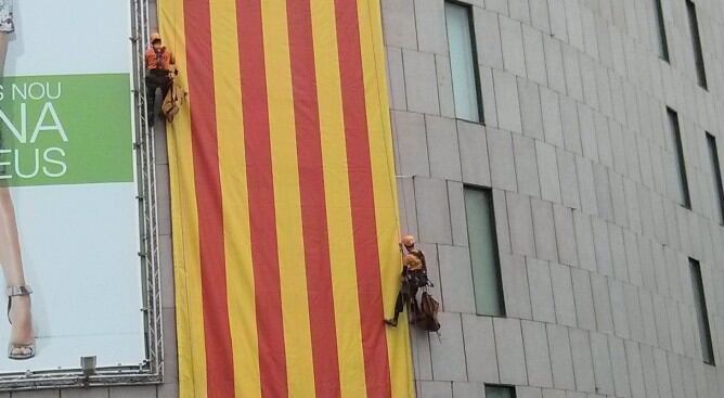 Uns operaris ajusten una monumental senyera a la façana de El Corte Inglés de Plaça Catalunya