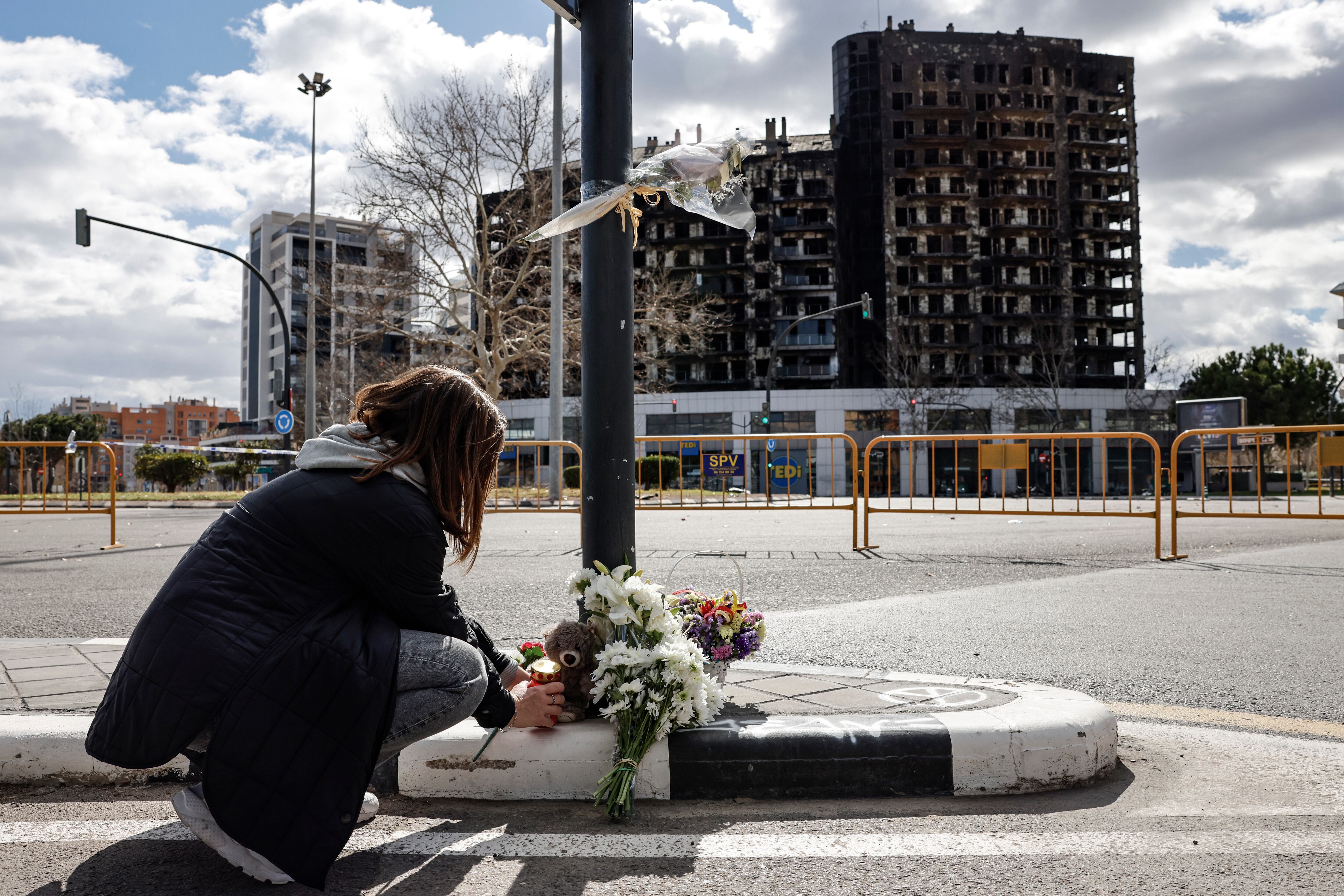 Una mujer deja un peluche, este sábado, junto a varios ramos de flores en recuerdo a las víctimas del incendio de un edificio en el barrio de Campanar de València que se ha cobrado la vida de al menos diez personas.